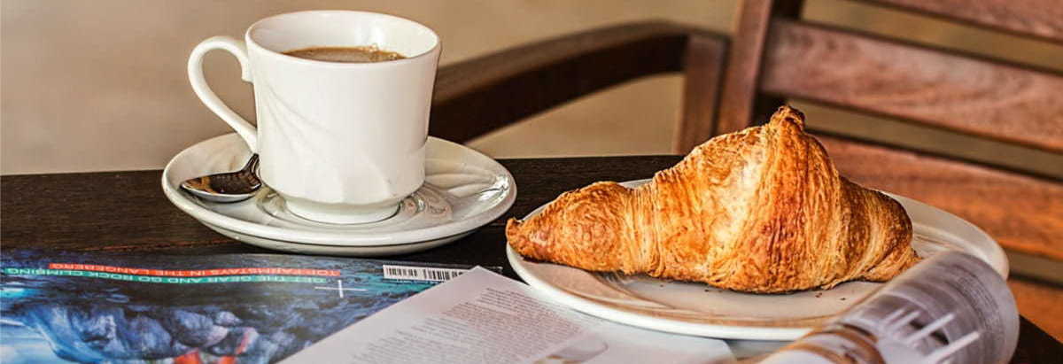 A magazine, tip of coffee and croissant